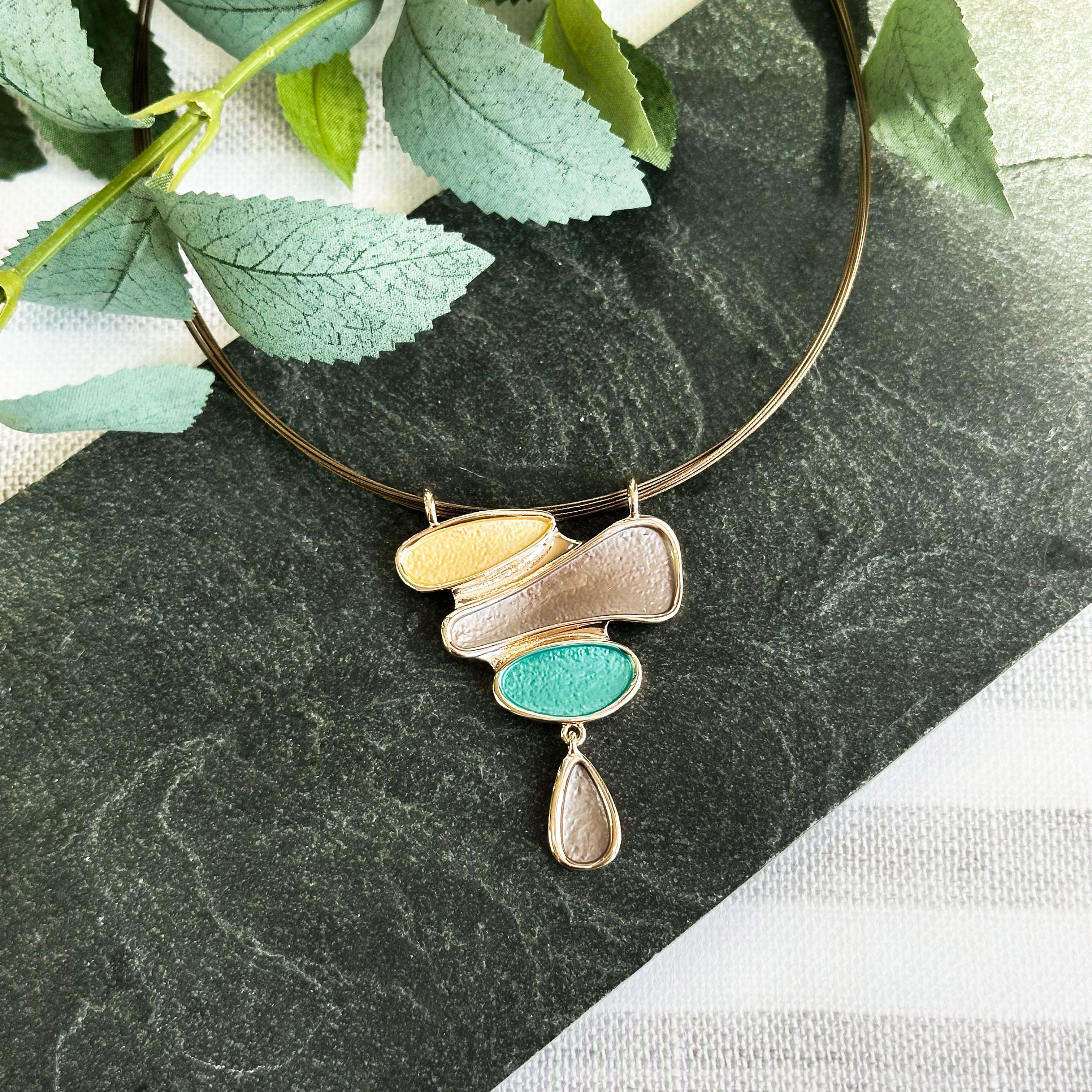 Necklace is a pendant with three organic shapes and a dangling teardrop painted in gold, brown, and teal. Necklace has a copper wire chain. abstract stacking stones drop pendant. nature inspired jewelry, geometric jewelry