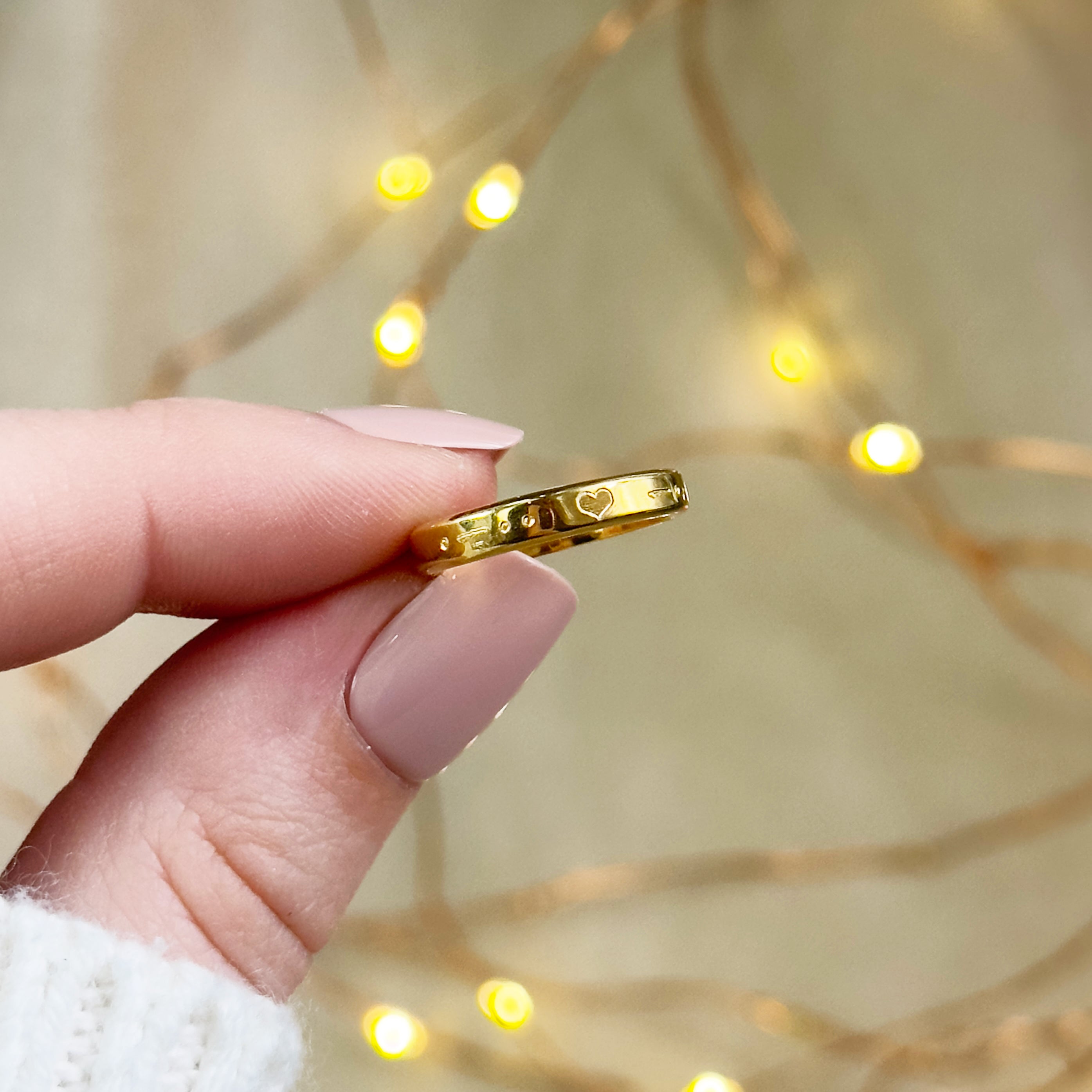 A person holds a dainty engraved 3mm gold ring with morse code initials separated by a tiny heart symbol. The ring is thin and dainty with custom engraving available. Personalized morse code ring, custom engraved secret code jewelry, secret code ring, custom secret message ring for couples, men and womens matching ring bands, couples initial rings