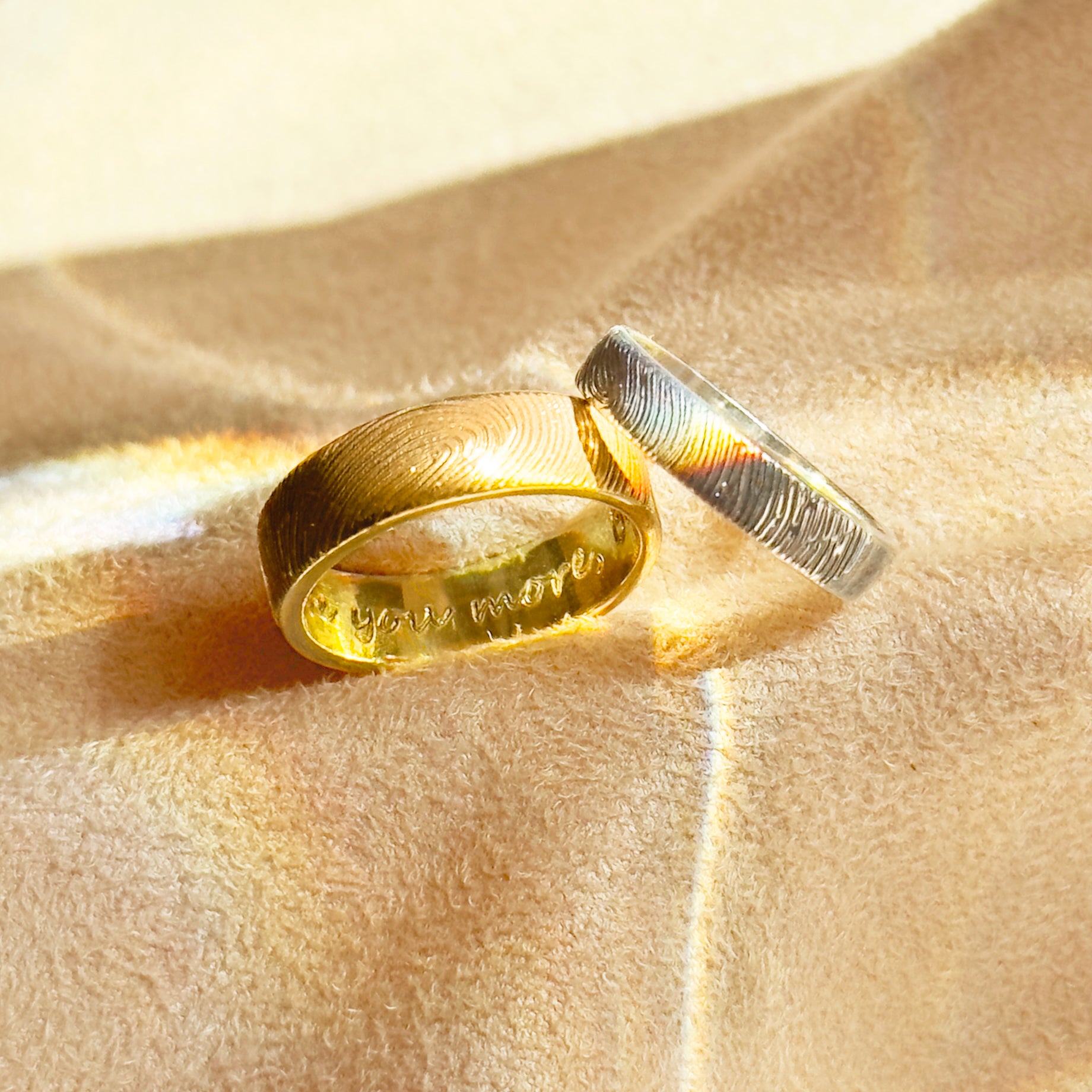 Custom fingerprint engraved rings in gold and silver displayed on soft fabric, featuring detailed fingerprint textures on the outside and a hidden engraved message inside. These unique personalized bands are perfect as his and hers wedding rings, memorial rings, or anniversary gifts. Crafted in high-quality sterling silver and gold vermeil, each ring is designed to capture the touch of a loved one, making it a timeless keepsake for couples, partners, or families.