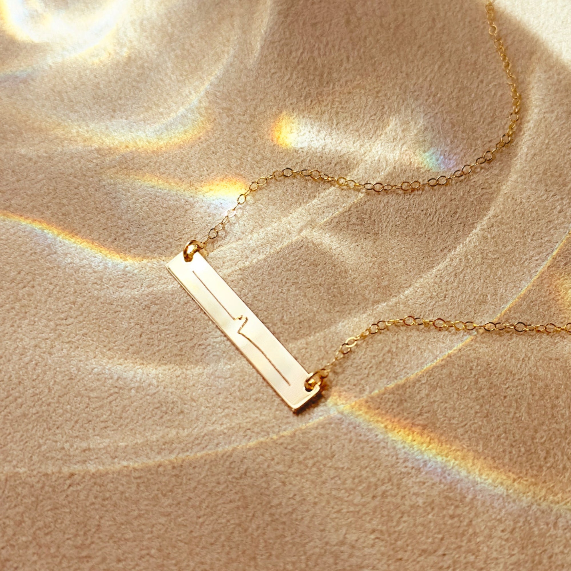 Gold-filled personalized heartbeat necklace shown flat with delicate chain and engraved bar pendant, perfect as a baby shower or miscarriage memorial gift, dainty and timeless.