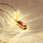 Gold necklace with a red ruby July birthstone bar pendant on a beige background
