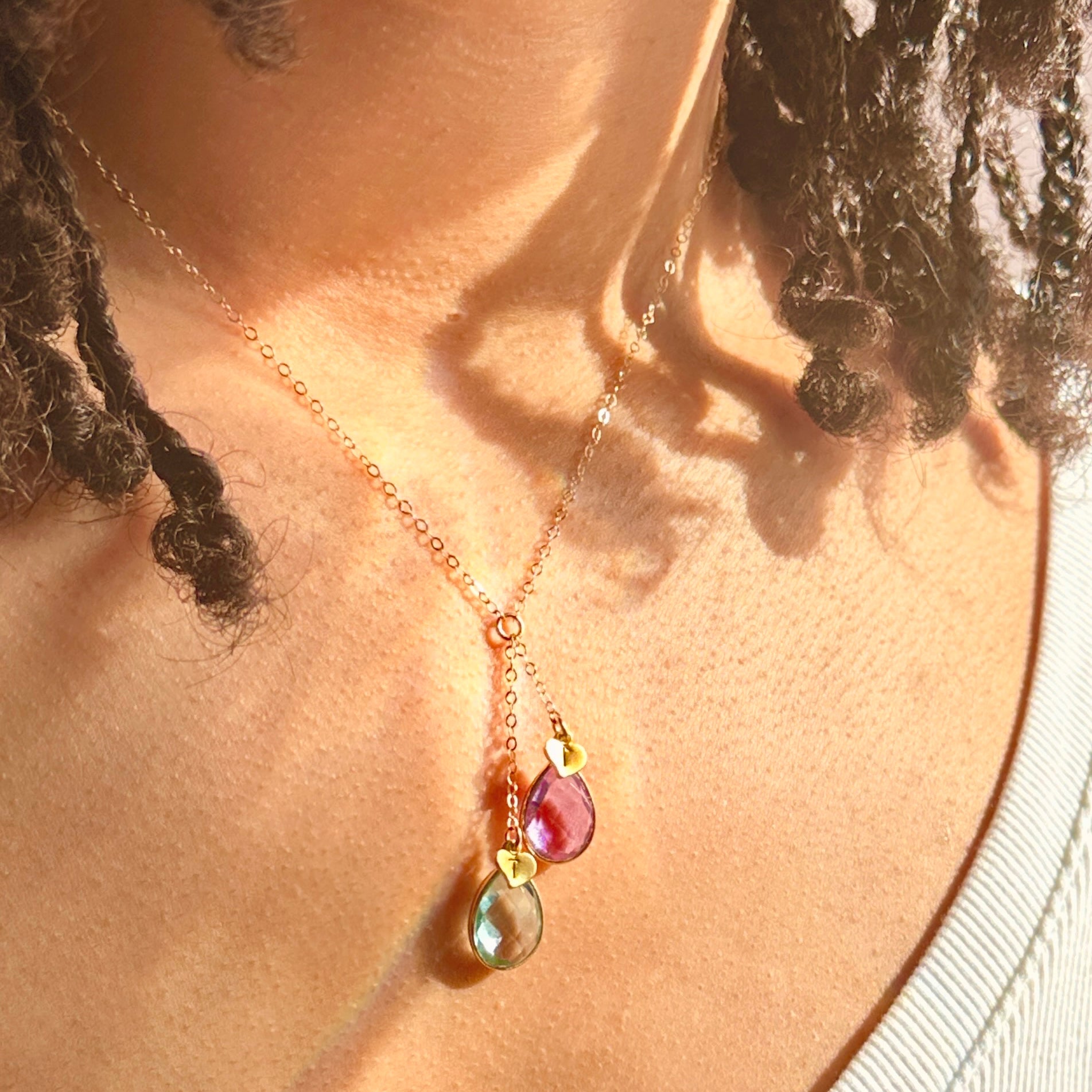 Model wearing gold two stone lariat necklace with ruby and blue topaz birthstones and hand stamped initial hearts. jewelry gift, necklace gift for her, anniversary gift, christmas gift, valentine's day gift, wedding jewelry, bridesmaid's jewelry, gift for mom, gift for wife, gift for girlfriend, gift for grandma, mother's day gift, july birthstone, december birthstone, birth month necklace, december necklace, july necklace
