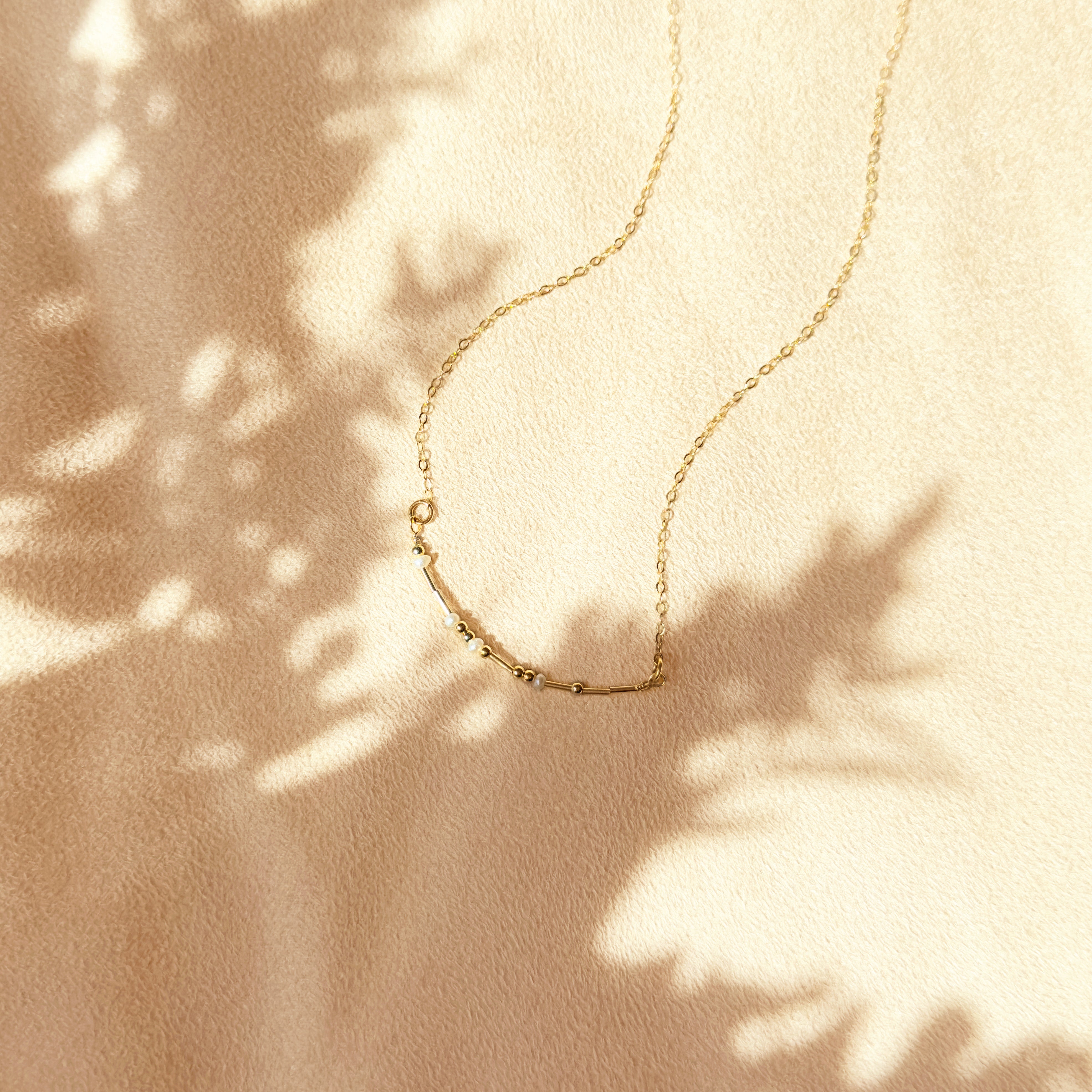 A gold morse code necklace with pearl spacers set on beige background. Couple gifts, couple initials, secret message gift, secret code gift, meaningful minimalist dainty necklaces for women, mothers day gift for her, personalized gift for women. Handmade beaded necklace gift. Custom beaded jewelry.