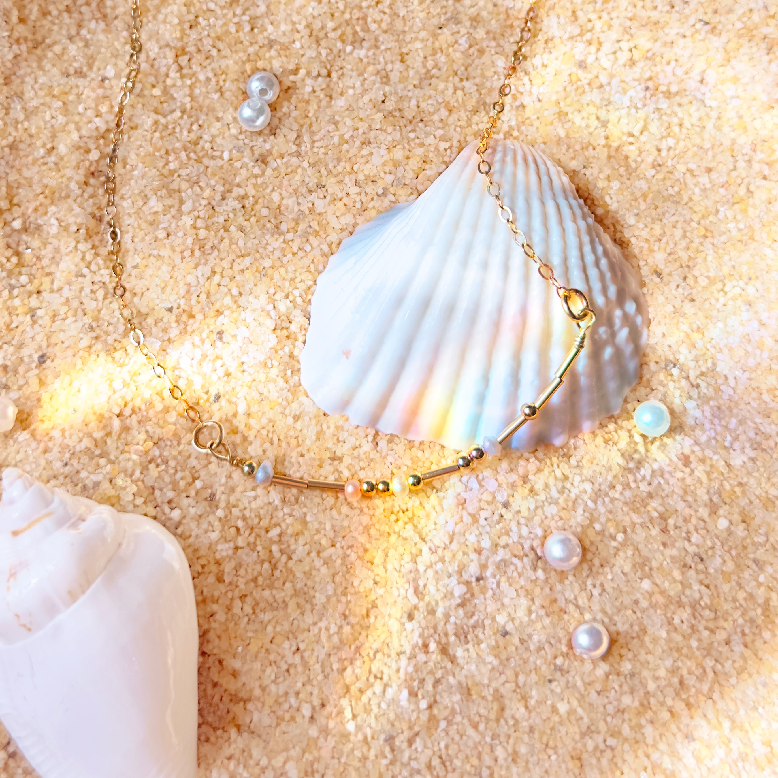 A gold morse code necklace with pearl spacers lays on top of a seashell. Couple gifts, couple initials, secret message gift, secret code gift, meaningful minimalist dainty necklaces for women, mothers day gift for her, personalized gift for women. Handmade beaded necklace gift. Custom beaded jewelry.