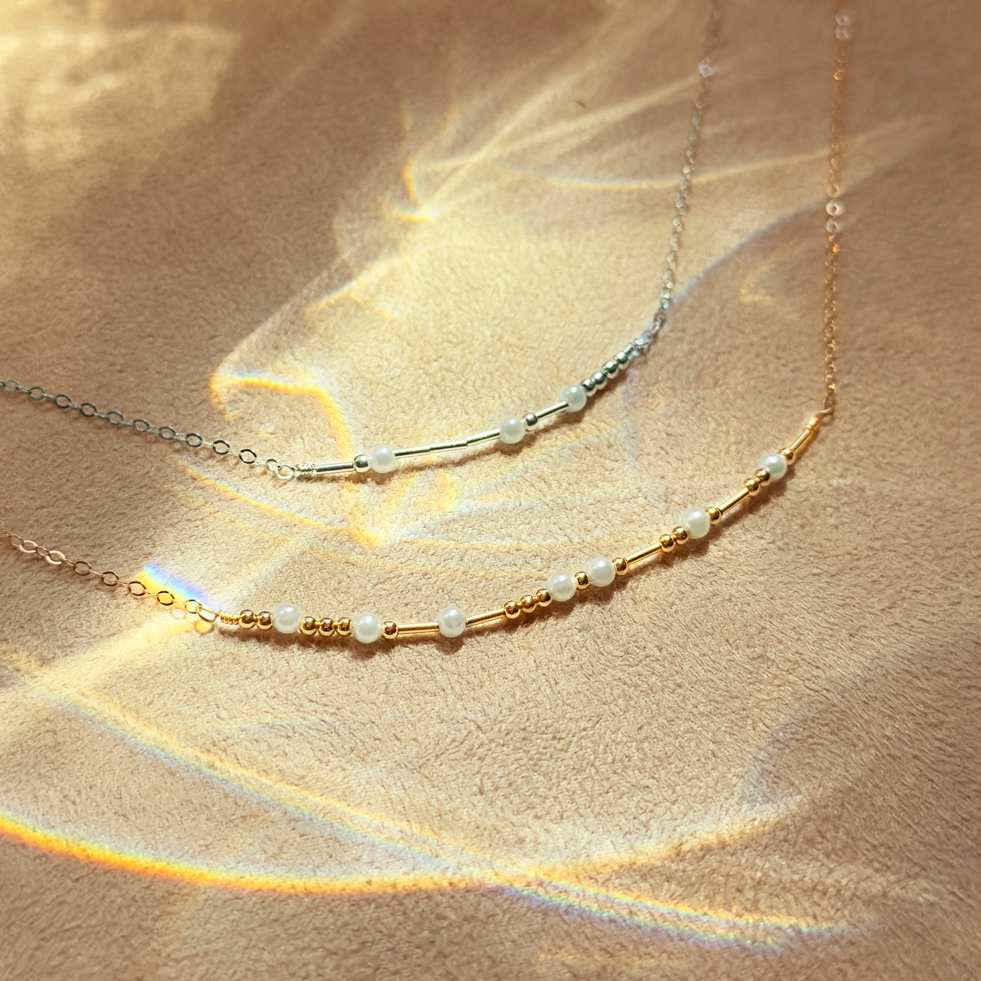Two minimalist morse code necklaces—one sterling silver, one gold filled—catch soft sunlight to highlight the bead pattern that spells a secret word. Perfect as a dainty layering necklace or bridesmaid gift, the adjustable chain sits gracefully at the clavicle. This morse code jewelry offers a modern, understated way to wear a personalized message while keeping the design simple, delicate, and ideal for everyday wear.