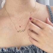 A person in a gray spaghetti strap shirt wears a horizontal zig zag birthstone necklace in gold. A zig zag birthstone necklace with a large mother's stone on the end rests in their hand in the sun against a white background. They show off a zig zag birthstone bracelet on their wrist against a white marbled background. They hold a pair of zig zag plus teardrop stud earrings. A pan over shot of the entire zig zag collection.  The Danique Jewelry Logo appears at the end of the video.