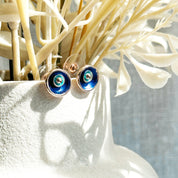 A pair of circular abstract flower earrings against a white background with rose gold plating and painted in blue and teal