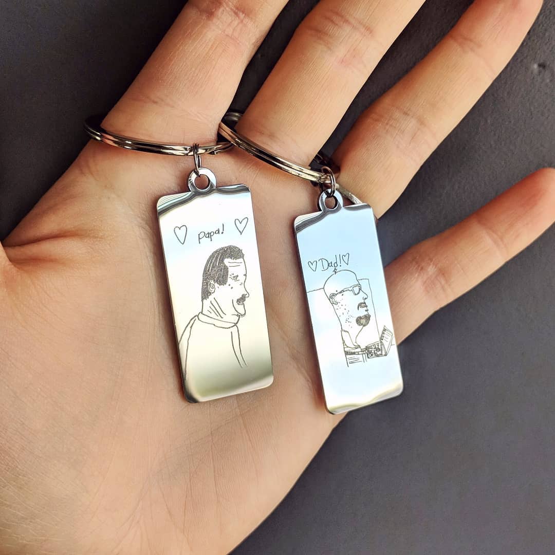Model is holding two rectangle keychains with child's drawing of dad and grandpa engraved. Perfect father's day, mother's day, birthday, celebration or for any holiday