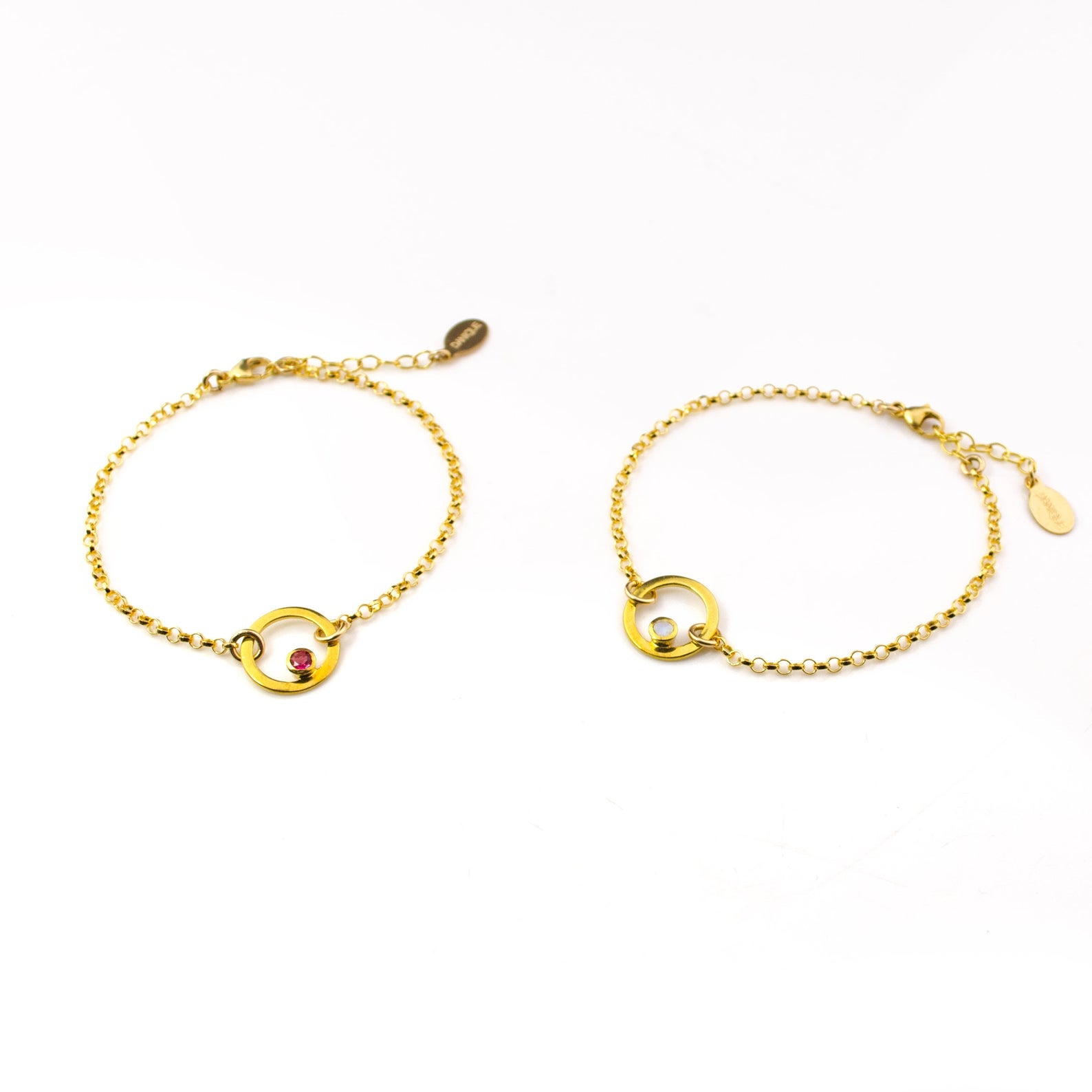 Two gold plated open circle pendant charm birthstone bracelets featuring  clear quartz and garnet birthstones. January birthstone, april birthstones. gemstone jewelry on white background.