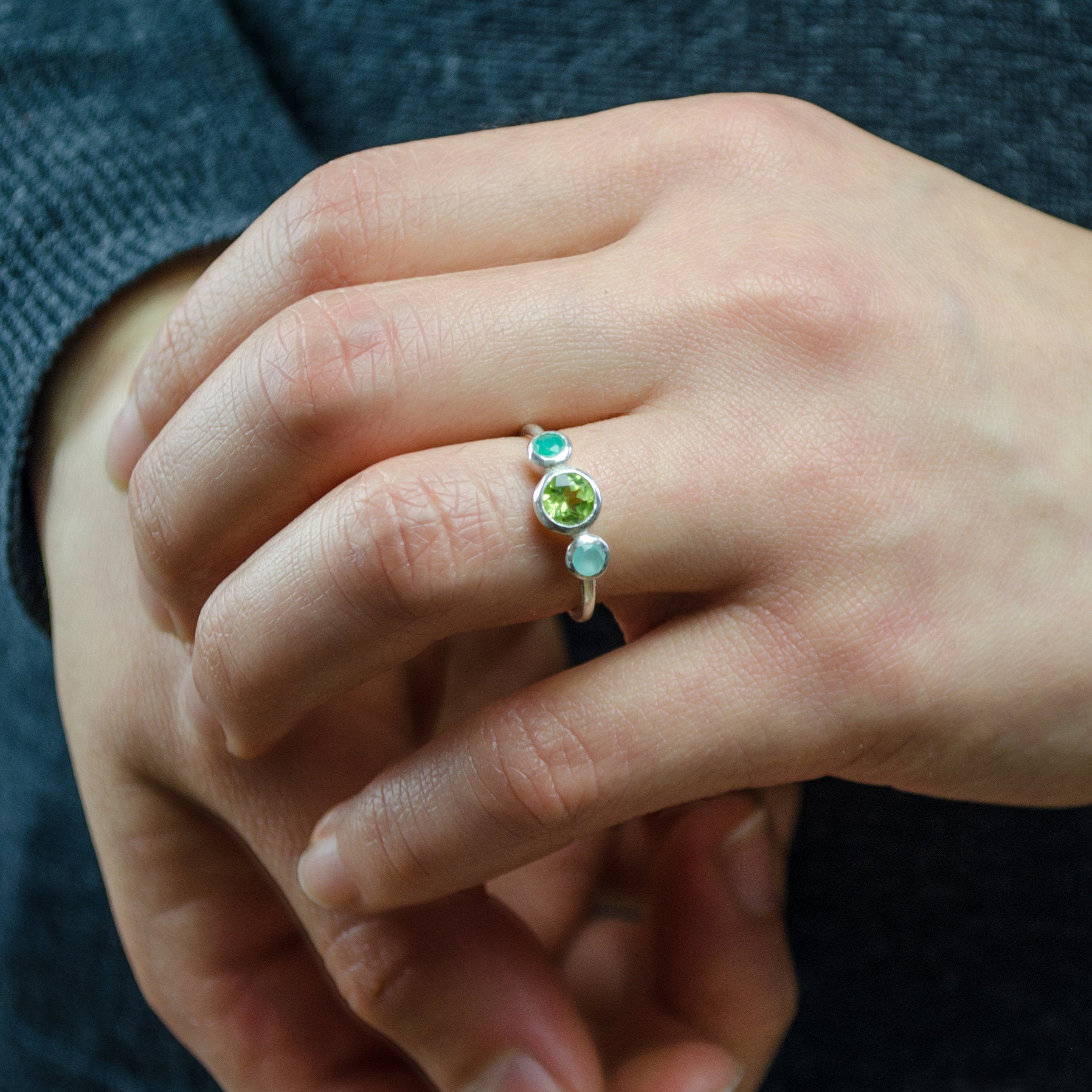 Model in a gray top is wearing the sterling silver mothers birthstone ring with a 5mm peridot gemstone and green onyx and aqua chalcedony kids birthstones.