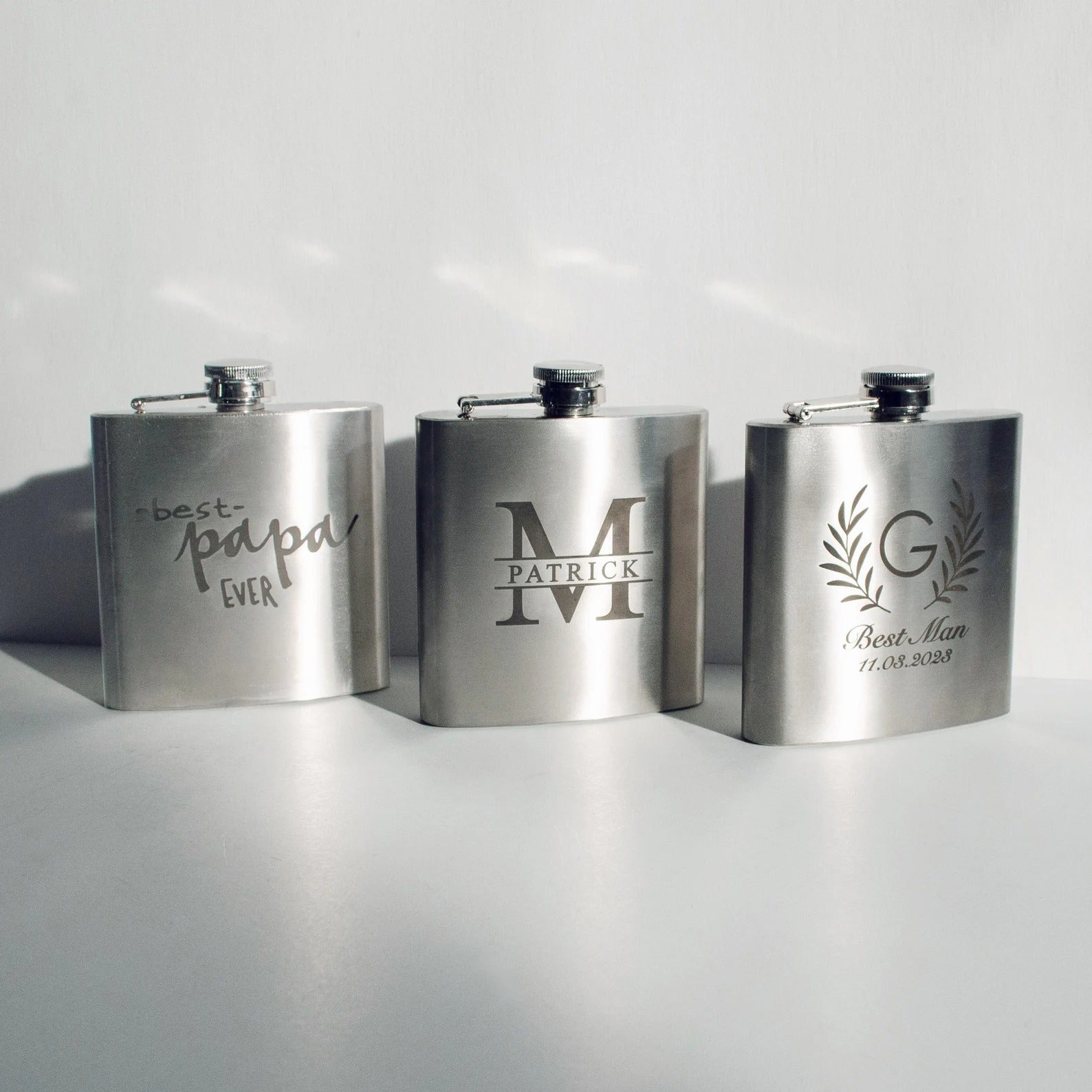 Three custom engraved stainless steel flasks in with different designs: name and message monogram, best man wreath design and best papa ever design. Fantastic personalized gift for party, wedding, christmas, birthday for dad, grandpa, husband or boyfriend.