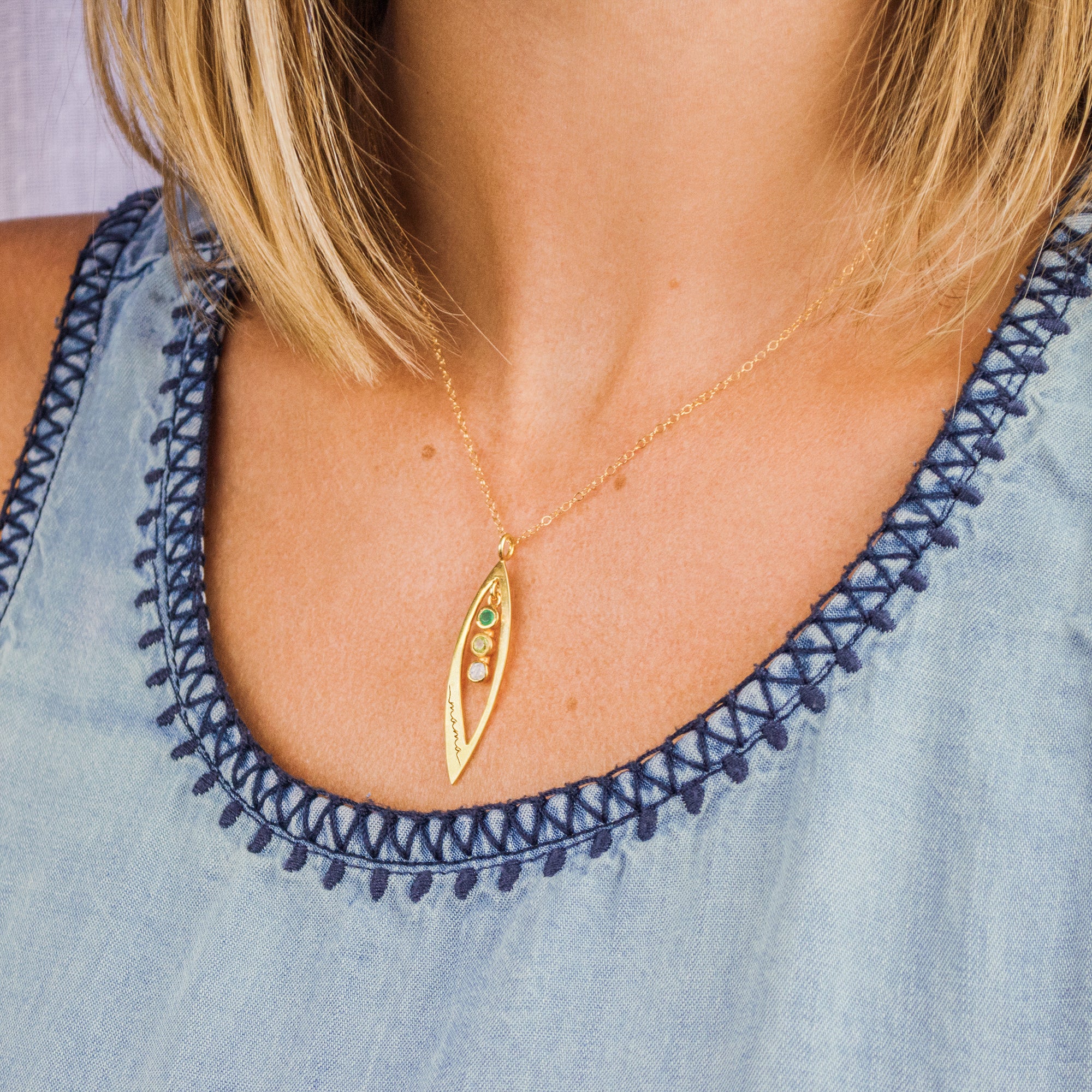 Model in blue top is wearing a gold filled mothers family tree necklace with open leaf pendant featuring green onyx, peridot and moonstone birthstones with mama design engraved.