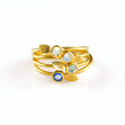Collection of four stacking leaf engraved initial 3mm birthstone rings in aqua chalcedony, clear quartz, moonstone and Iolite in gold.