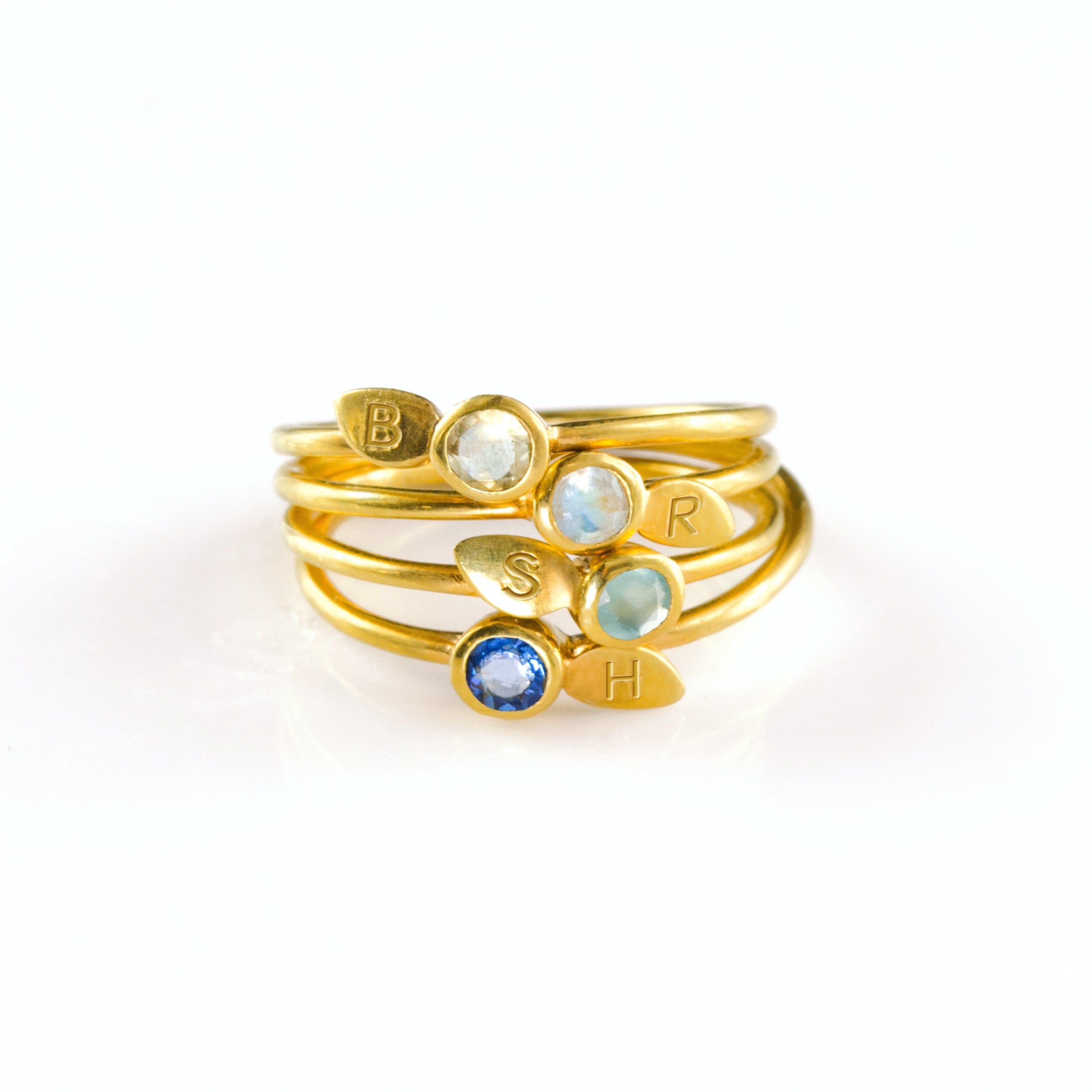 Collection of four stacking leaf engraved initial 3mm birthstone rings in aqua chalcedony, clear quartz, moonstone and Iolite in gold.