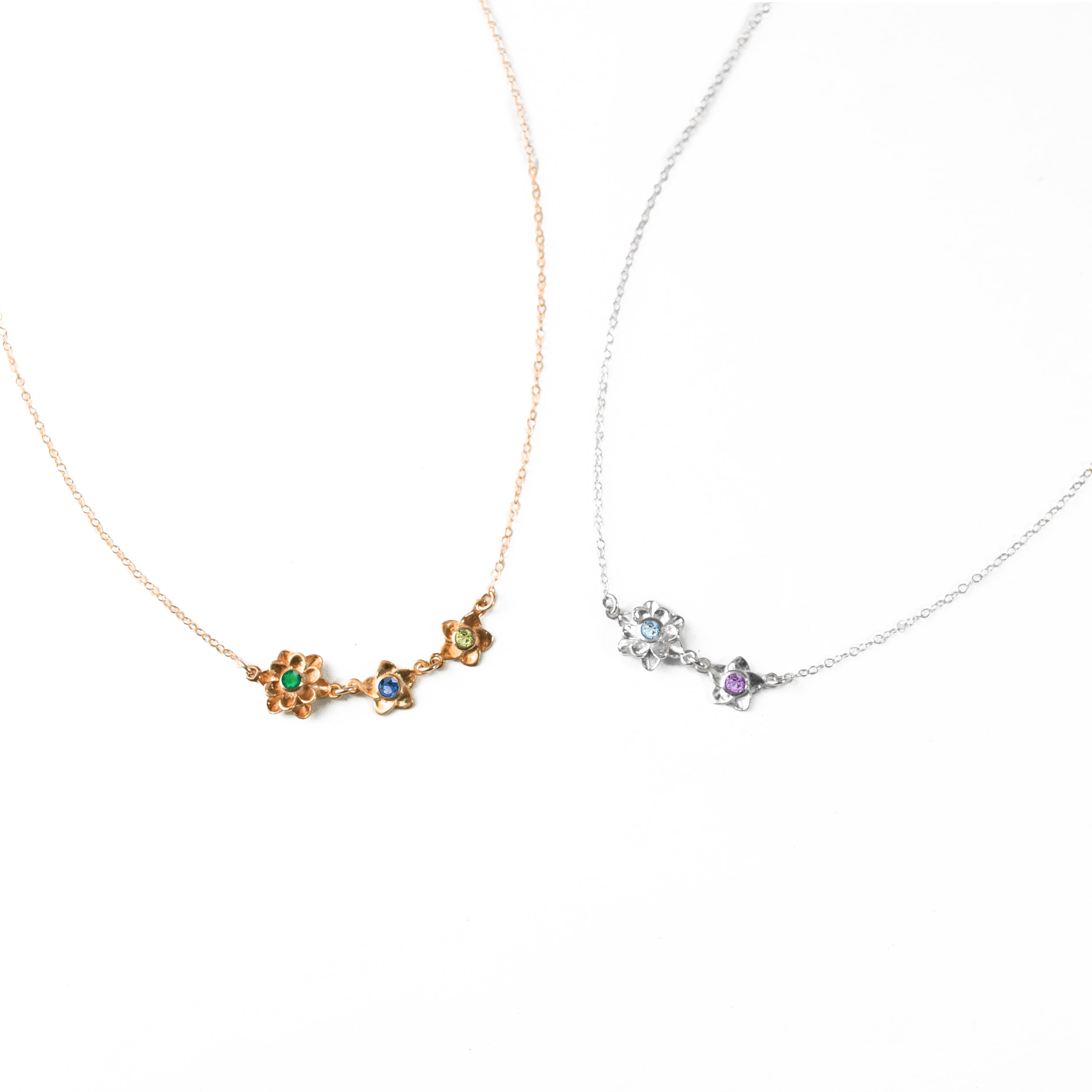 Rose gold mom of two bloom necklace with green onyx, kyanite and peridot birthstones. Sterling silver mom of one bloom necklace with sky blue and purple amethyst birthstones on a white background.