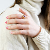 Model in white sweater is wearing a gold plated Oval purple turquoise ring  birthstone ring, gemstone, Bezel set, Sterling silver or gold, purple faceted ring, gift, ring.