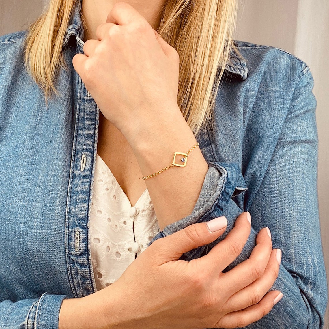 Model in white top with jean jacket is wearing the open square geometric birthstone bracelet in gold filled with kyanite birthstone.