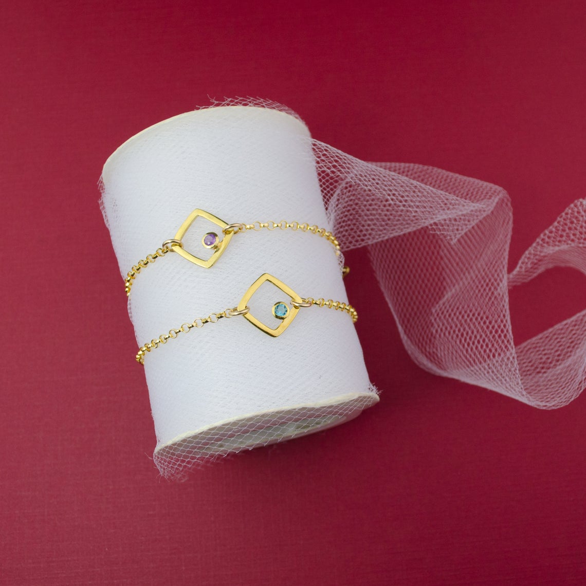 Two gold open square geometric bracelet with purple amethyst and blue quartz birthstones.