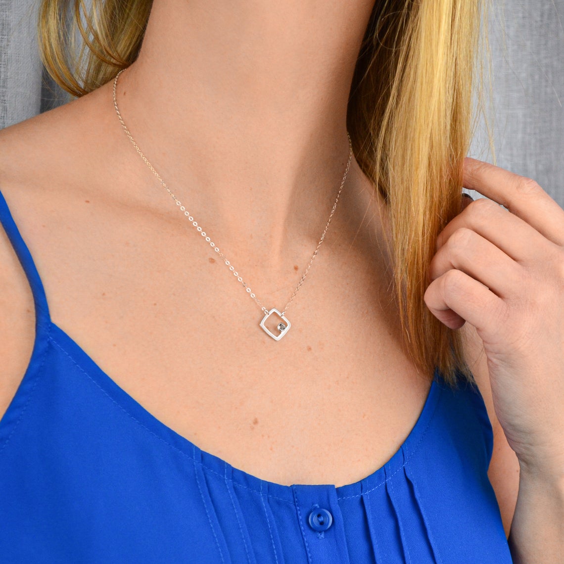 Model in blue top is wearing a sterling silver open square minimalist necklace with iolite birthstone september birthstone.