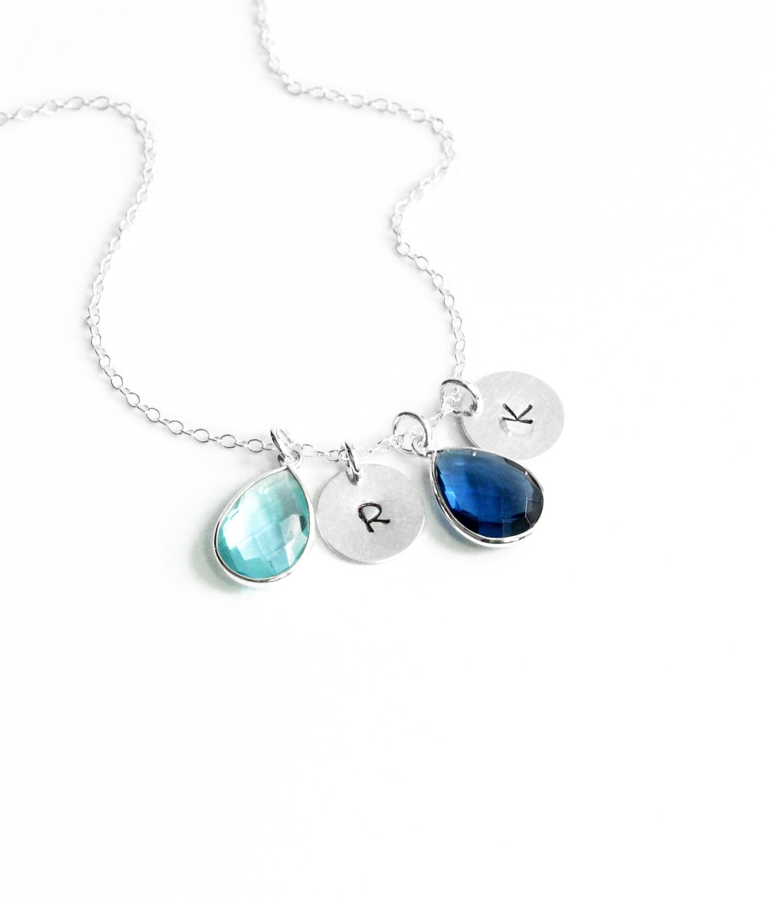 Sterling silver cable chain teardrop hand stamped polished disk initial necklace with sky blue topaz and kyanite birthstones on white background.