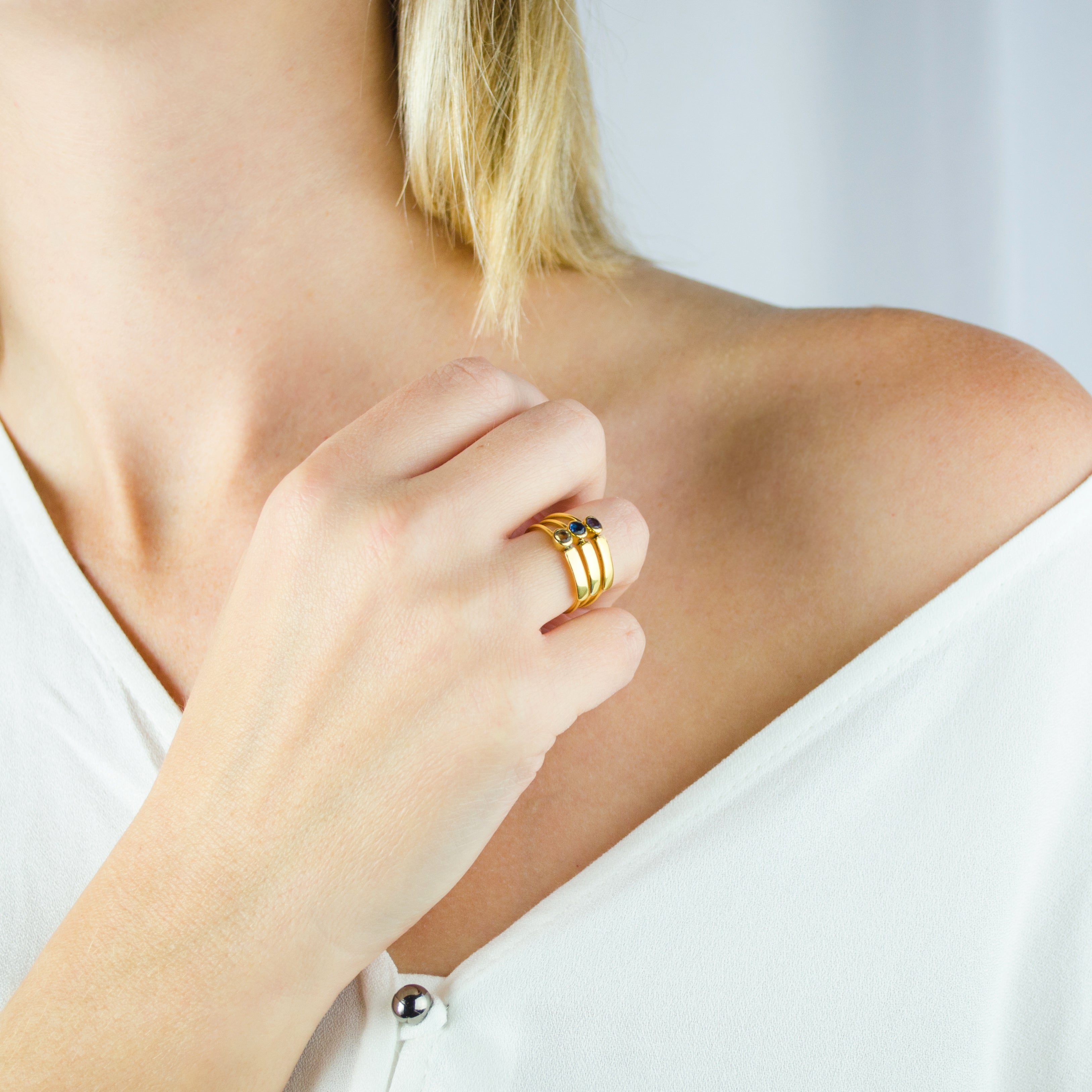 Model in white top is wearing a collection of three stacking rings gold plated name bar rings with purple amethyst, iolite, and peridot birthstones. engraved name ring, birthstone jewelry, birthstone ring