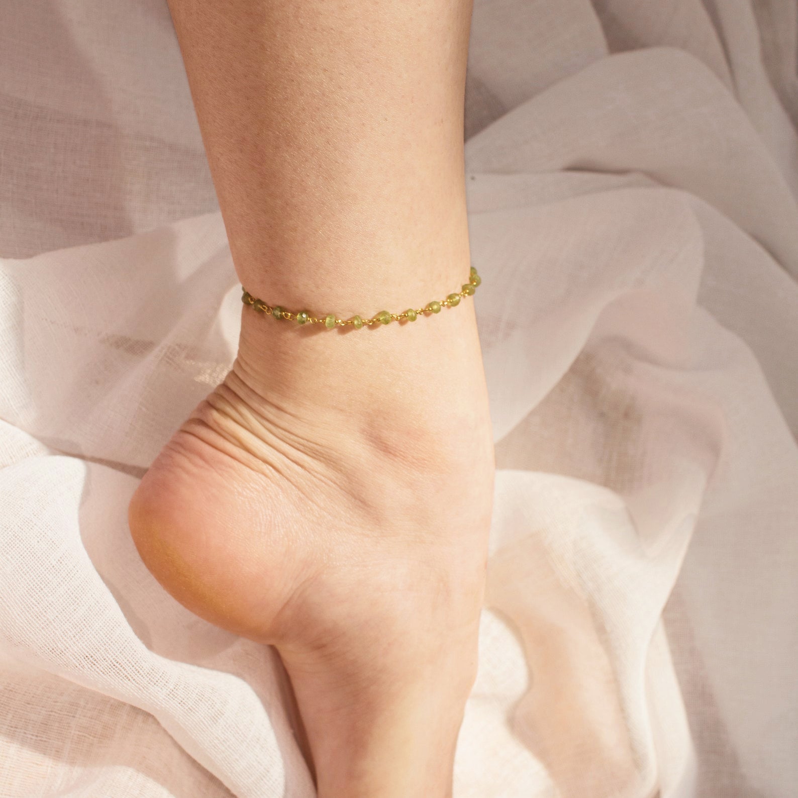 Model is wearing a gold filled wire wrapped peridot or August birth month anklet.