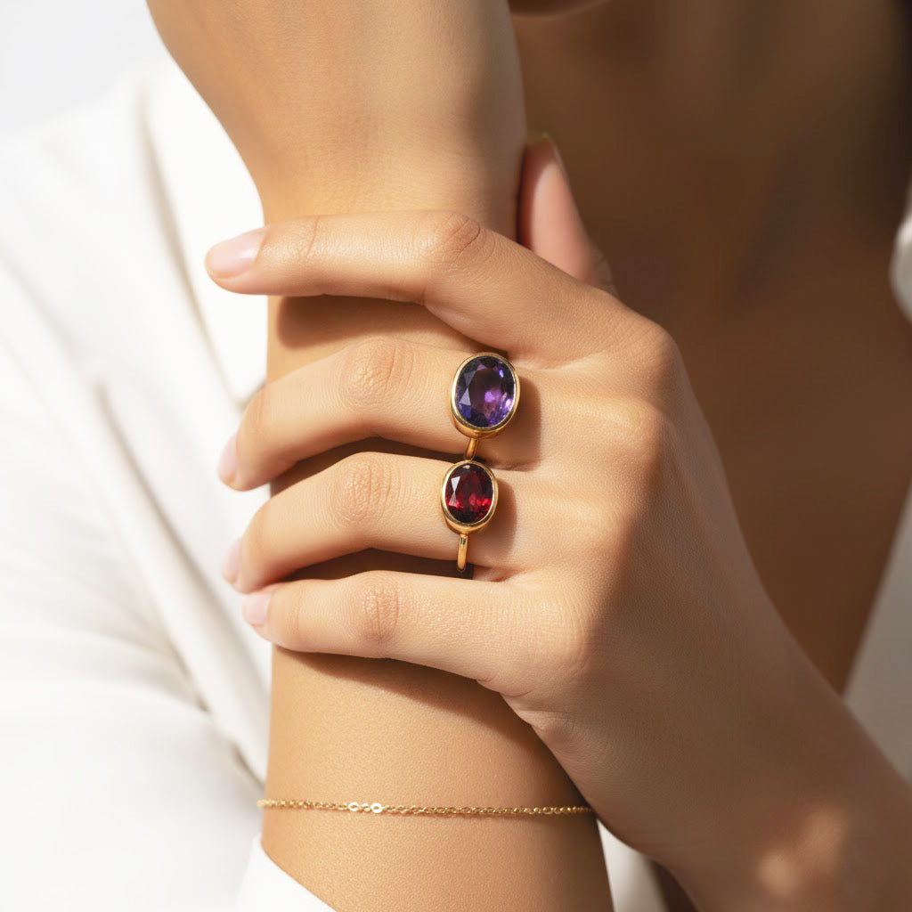 Minimalist oval gemstone stacking rings with amethyst and garnet set in gold bands worn on a model’s hand, elegant colorful stacking ring jewelry styling, delicate birthstone ring stack for women