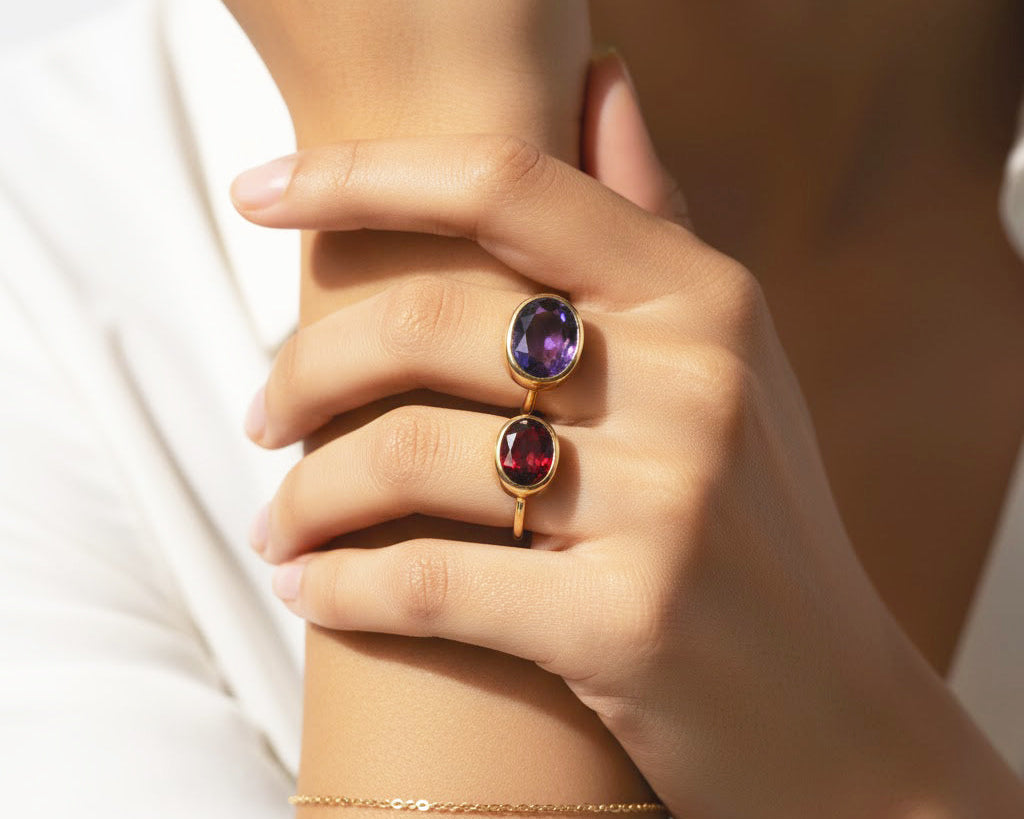 Minimalist oval gemstone stacking rings with amethyst and garnet set in gold bands worn on a model’s hand, elegant colorful stacking ring jewelry styling, delicate birthstone ring stack for women