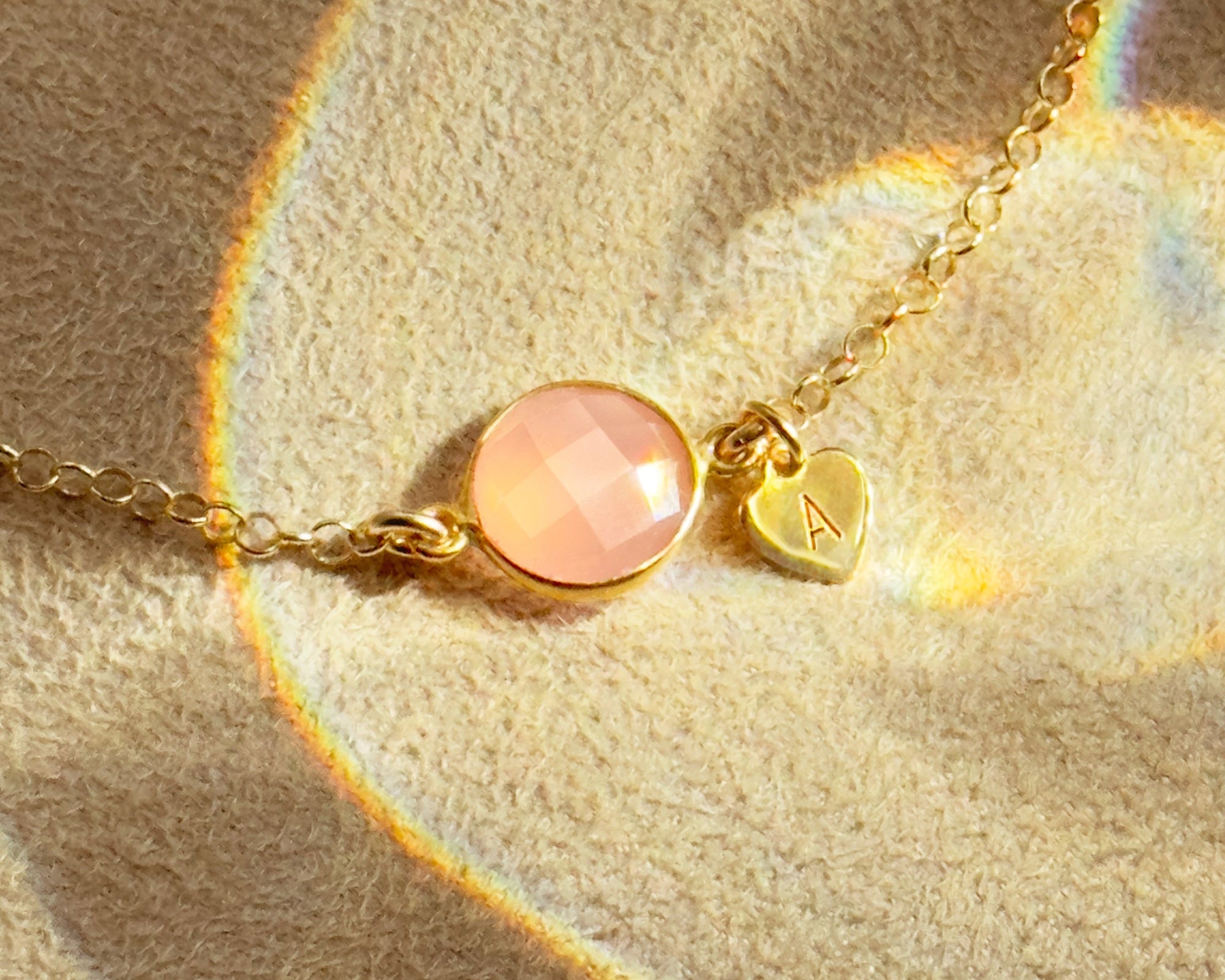 Delicate gold bracelet with faceted pink chalcedony October birthstone and personalized heart charm engraved with initial, dainty handmade jewelry gift for mom, daughter, or best friend.