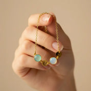 Mom’s custom birthstone initial bracelet held delicately between fingers, featuring a dainty gold chain with pastel bezel-set gemstones and tiny round letter discs spelling children’s initials for a meaningful family design. Minimalist personalized bracelet perfect for everyday wear or stacking with other bangles, a sentimental Mother’s Day, birthday, Christmas or new mom gift celebrating kids’ birthstones and initials in elegant, modern style.