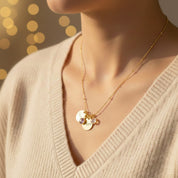 A woman wearing a personalized birthstone disc charm necklace with a 13mm engraved disc and 6mm birthstone charm, shown on a delicate gold chain. Customizable with initials, names, or dates, this dainty necklace makes a meaningful gift for mom, grandma, best friend, bridesmaids, or new moms, and layers beautifully with other minimalist jewelry styles.
