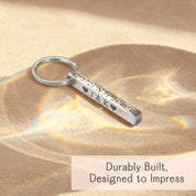 Close-up of a silver stainless steel 3D bar keychain resting in warm light, showing crisp laser engraving along the edge. Minimalist style highlights reflective finish, readable lettering, and modern proportions—great for roman numeral keychain or latitude/longitude GPS coordinates gift; durable everyday carry accessory for him or her.