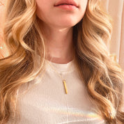 Model in beige top is wearing the gold plated daitny 3d bar necklace with script engraving on a cable chain. necklaces for women, gift for her, gift for wife, birthday, christmas gift, valentine's day gift, gift for girlfriend, anniversary gift, silver anniversary, gold anniversary, personalized jewelry, custom jewelry, gift for fiance, holiday gift, unique gift ideas, necklaces for her, wedding party gifts, bridal party gifts, prom season, prom jewelry, birthstone necklaces, engraved necklaces, grad gift.