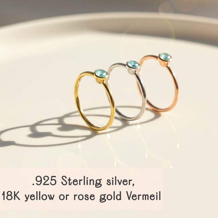 set of dainty stackable gemstone rings displayed on soft champagne satin fabric, featuring aqua chalcedony and other birthstones bezel set in thin gold vermeil bands, highlighting the elegant minimalist design ideal for stacking or wearing alone, available in all birthstones for custom mom ring stacks or meaningful birthday gifts, handcrafted in sterling silver or gold vermeil with delicate round stones perfect for everyday wear or special gifting