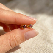 Hand holding tiny birthstone stud earrings showing small scale and delicate bezel set gemstone design