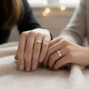 Two people resting hands together on a soft blanket, each wearing a slim silver engraved ring, cozy lifestyle photo showcasing matching personalized bands, custom name or message rings for best friends, sisters or couples, meaningful promise ring gift for her, minimalist everyday jewelry.