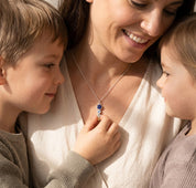 Mom wearing a custom birthstone necklace with her children, showing a sentimental family necklace made with birthstones for loved ones.