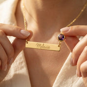 Gold engraved name bar necklace with Melanie and purple round birthstone worn by woman