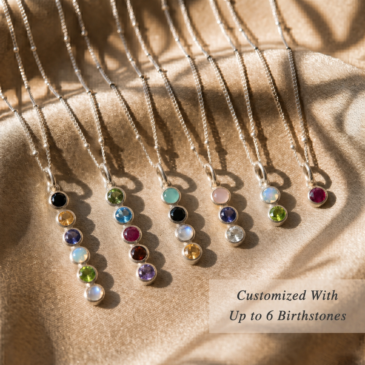 Necklaces with birthstones on a beige fabric background. Each birthstone necklace features between 1 and 6 birthstones to represent mothers and grandmothers of one, two, three, up to six. 