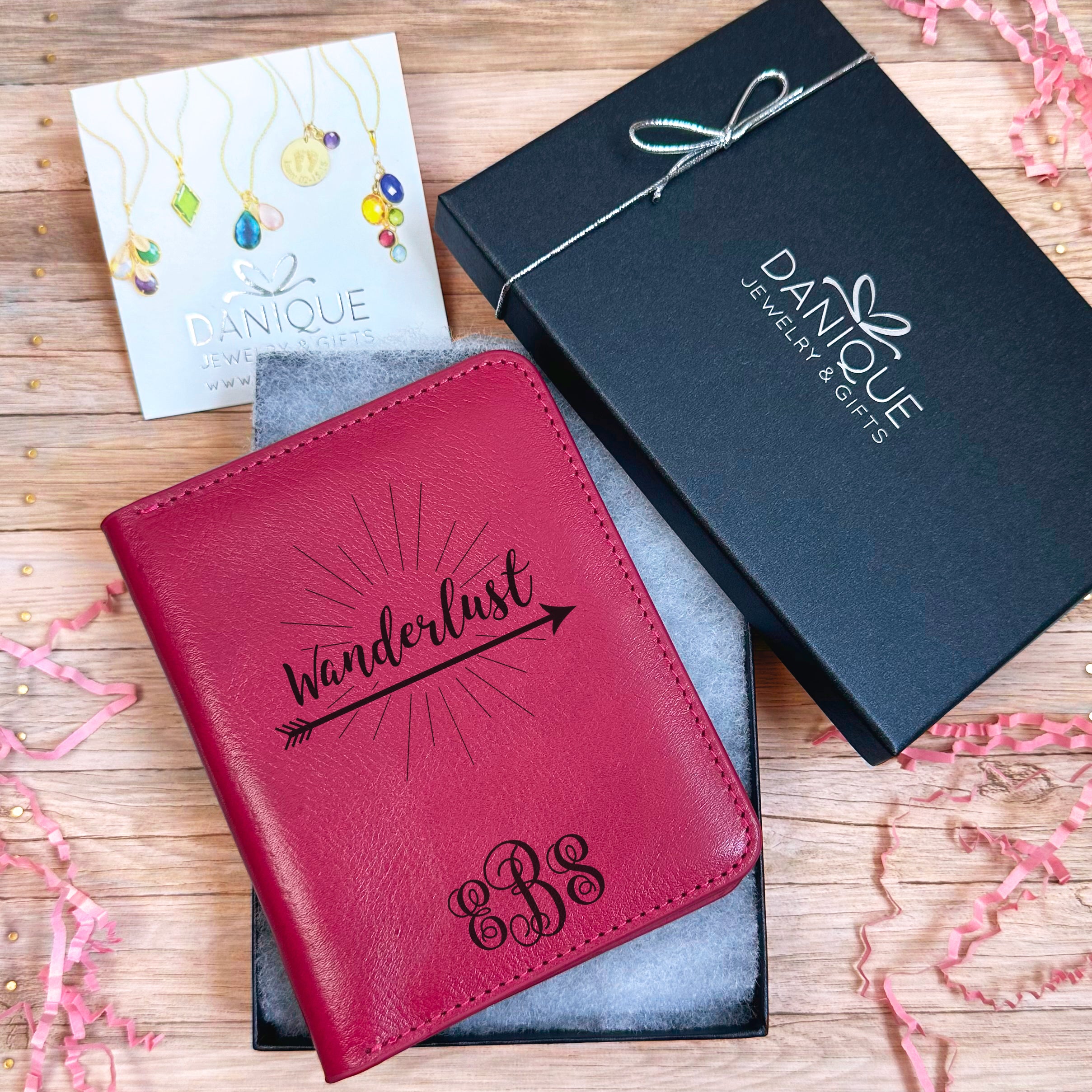 A Raspberry passport holder with the word Wanderlust resting over an arrow and a Swirly Monogram with initials EBS sits in an open Danique Jewelry box. Ready for Gifting Passport Holder with Custom Design and Natural Organic Leather Material in Danique Jewelry gift box. Gift ready. gifting ready, gift giving ready
