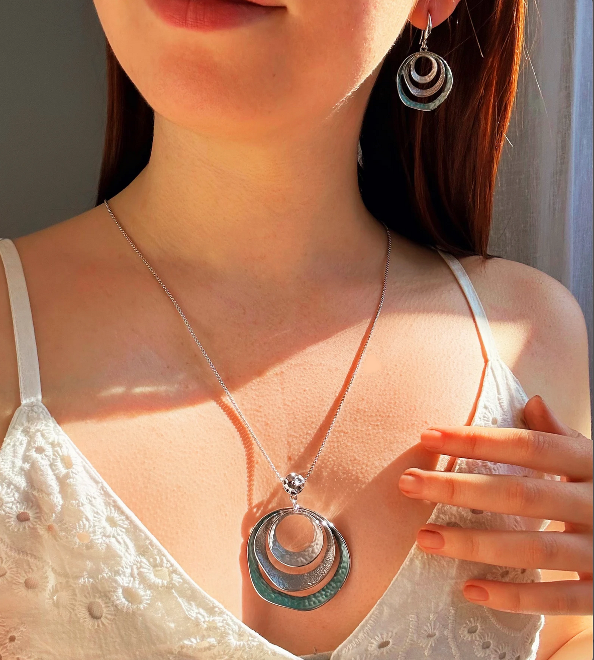 Model in white top is wearing the beautiful three circles statement necklace and earrings set with silver and blue tones. Necklace is made with a steel cable chain and a zinc alloy pendant with a galvanic finish. 