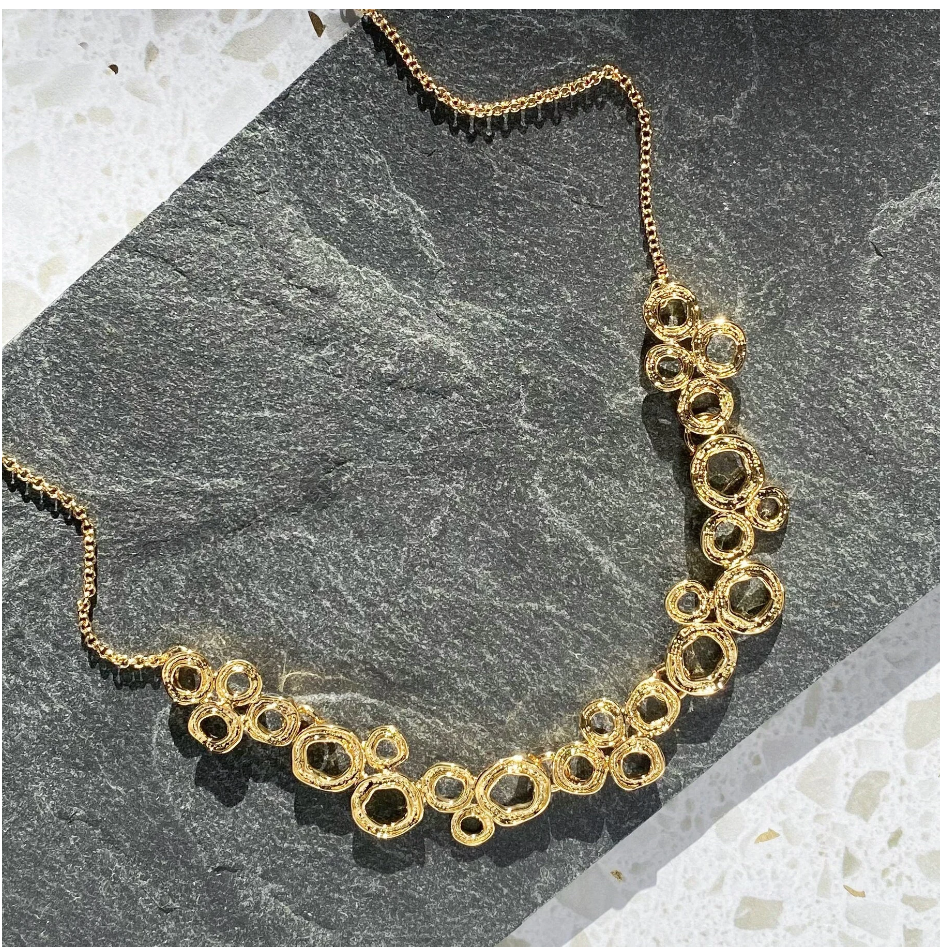 A gold necklace with a chain and a pendant made of multiple interconnected circle set on stone. connected circles, adjustable necklace, zinc alloy, push back earrings, stud earrings, geometric jewelry, geometric necklace, statement necklace, boho jewelry, boho necklace, bohemian jewelry, bohemian necklace, mother's day gift for her, christmas gift, custom jewelry, valentine's day gift, birthday gift for mom, gift for her, nature inspired jewelry, fashion jewelry, stud earrings, push back earring