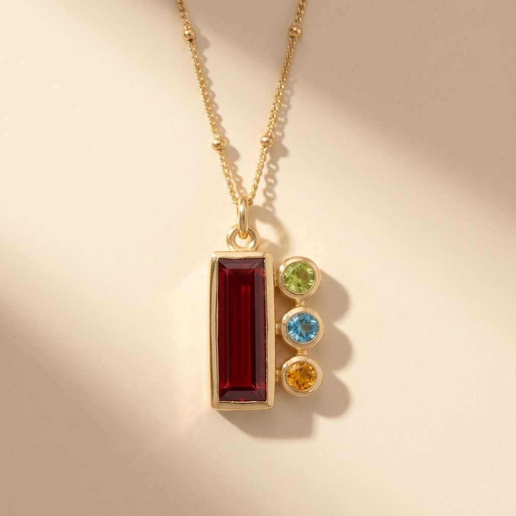Custom birthstone necklace for mom featuring a red baguette birthstone pendant with three tiny kids’ birthstone charms on a delicate gold chain.