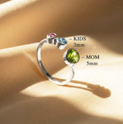 Mother’s birthstone ring showing larger center stone for mom and smaller stones for kids, personalized gold family ring with ruby, sapphire, and peridot, adjustable custom jewelry gift for mothers of multiple children.