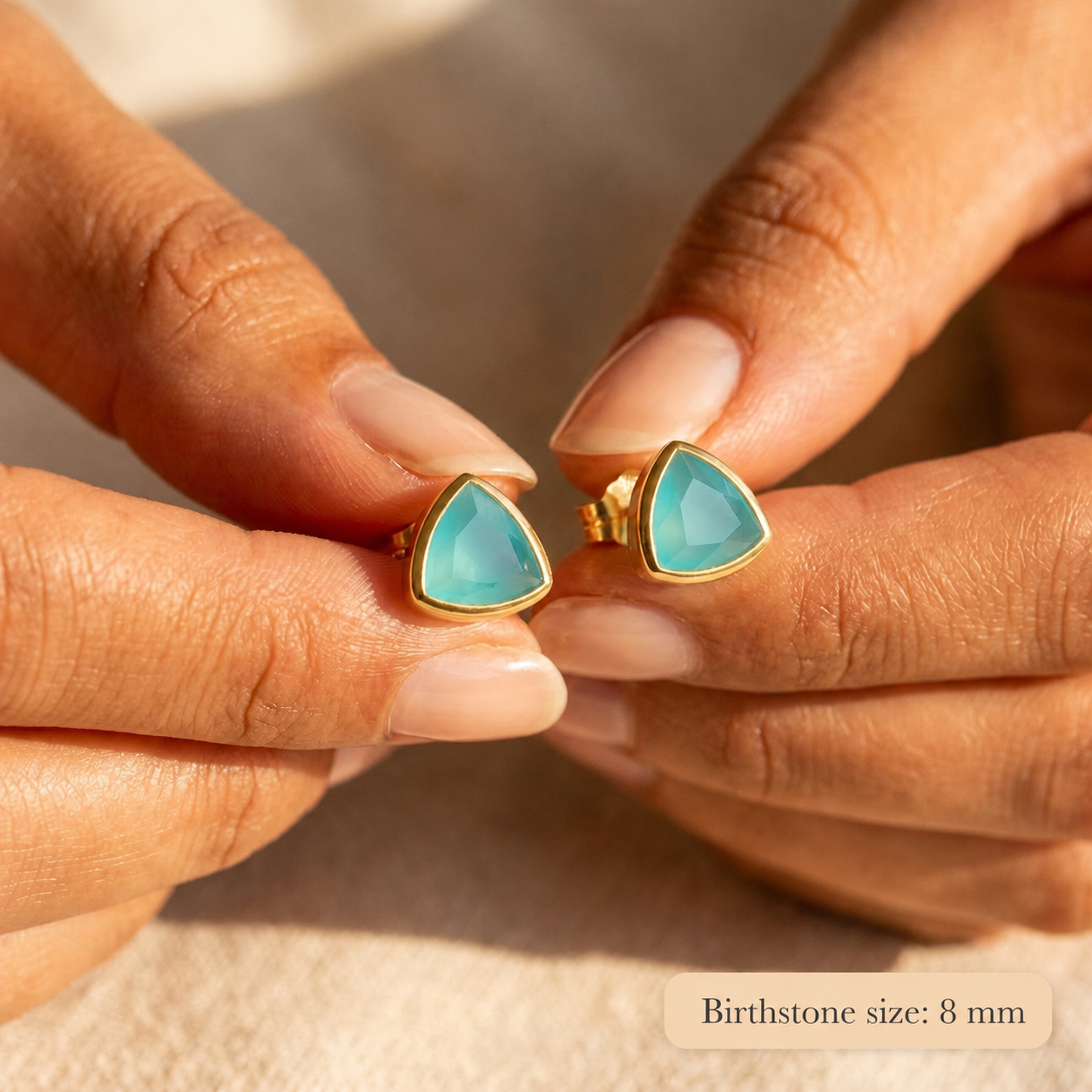 Aqua chalcedony triangle stud earrings held between fingers, showing the 8mm blue-green gemstones in gold settings.
