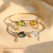 Two birthstone bangle bracelet with teardrop gemstones and initial charms, available in gold and sterling silver for a personalized gift.
