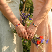 Two birthstone bangle bracelet worn outdoors on bridesmaids with flowers, a dainty custom gemstone cuff for bridesmaids, sisters, or gifts for her.