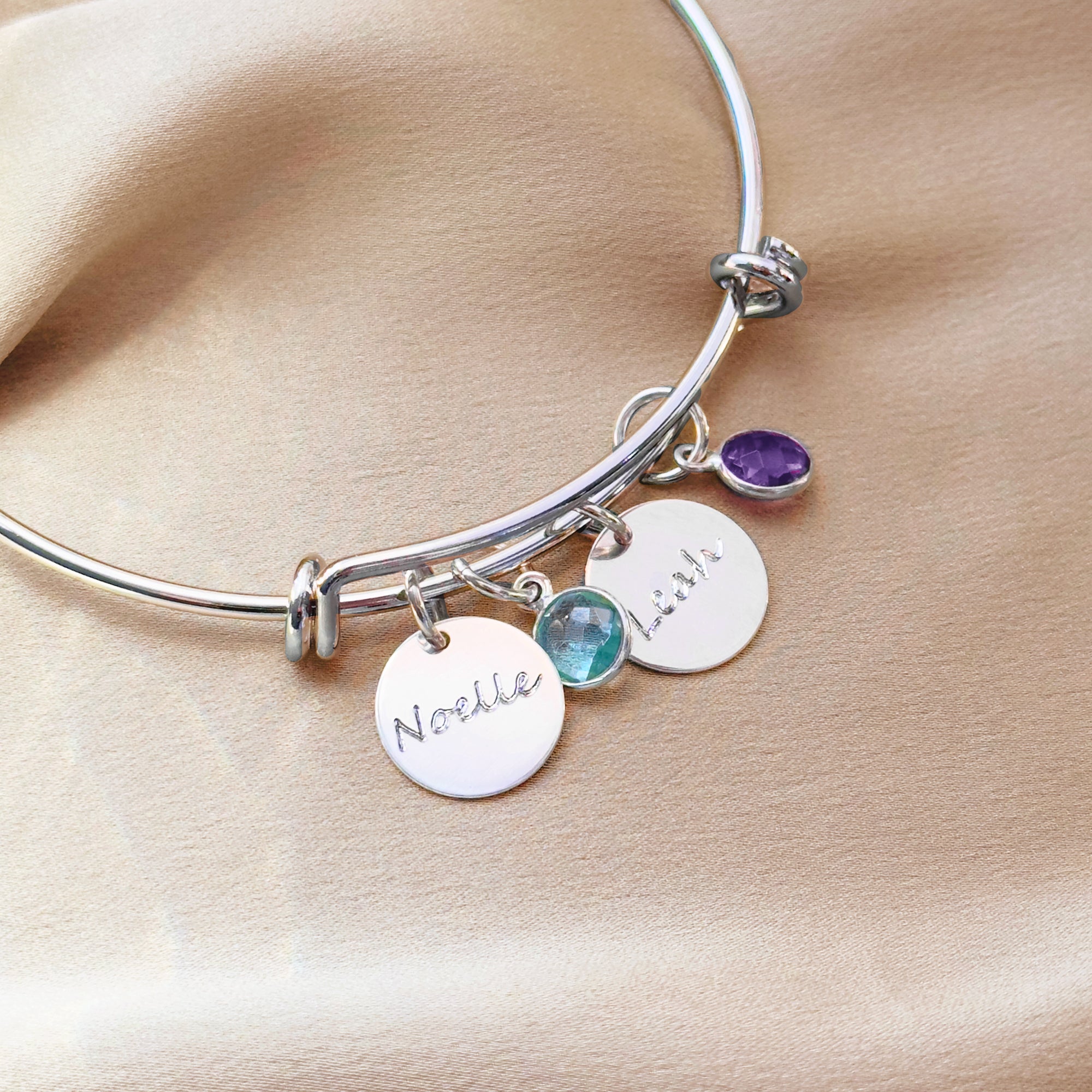 Sterling silver personalized birthstone bangle bracelet with engraved name discs and bezel-set tiny round birthstones representing children. Custom family bracelet offering name, initial, or date engraving plus optional back engraving. A meaningful Christmas gift for mom, Mother’s Day gift, or grandma keepsake featuring garnet, amethyst, aquamarine, peridot, ruby, citrine, moonstone, and blue topaz charms handcrafted in a minimalist adjustable design.