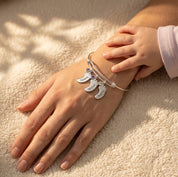Silver footprint charm bangle bracelet worn on wrist, personalized with children’s names and tiny birthstone charms.