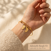 Woman wearing a gold personalized footprint bangle bracelet with engraved name charms, shown as a sentimental mom gift.